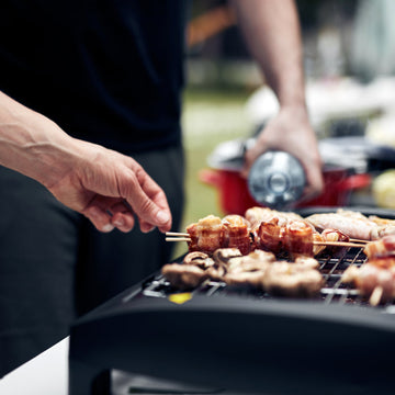 Bacon-wrapped skewers and mushrooms cooking on a compact tabletop grill for outdoor BBQ beginners in Winnipeg.