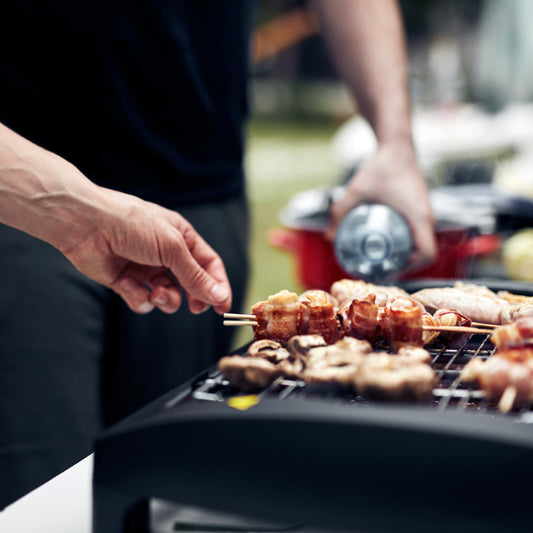 Bacon-wrapped skewers and mushrooms cooking on a compact tabletop grill for outdoor BBQ beginners in Winnipeg.